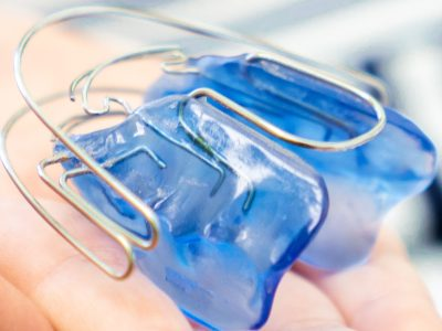 Removable blue acrylic retention appliance with wire elements, held in hand
